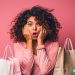 A woman holding shopping bags against a pink background. She has a distressed look on her face.