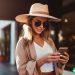 A woman wearing a sunhat on a city street looking at her phone.