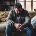 A depressed looking man sitting at home alone in his living room