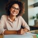 A woman with glasses on a vibrant smile and a pen in her hand.