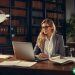 A blogger sitting at her a desk in a library surrounded by legal texts.