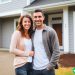 A couple in their early thirties standing in front of their new house that they just bought.