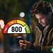 A man wearing a coat and looking down at his phone. There is a credit score graphic overlaid on top of the image, showing that 800 is a very high credit score.