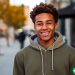 A young man in his early twenties that is standing on the sidewalk and looking and smiling at the camera.
