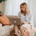 A woman blogging on her laptop while she is sitting on her couch in her living room.