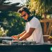 A man working a DJ booth at an outdoor venue as a side hustle.