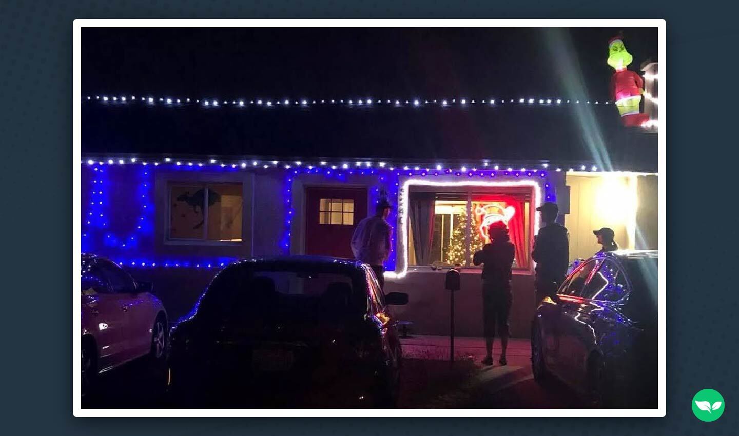 A one-story home decorated with blue and white Christmas lights, with several silhouetted people gathered out front admiring the display.