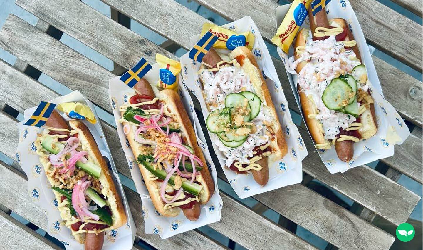 Overhead view of four Swedish-inspired hot dogs from Chef Hej Hej, topped with shrimp salad, pickled vegetables, mustard, and mini Swedish flags.