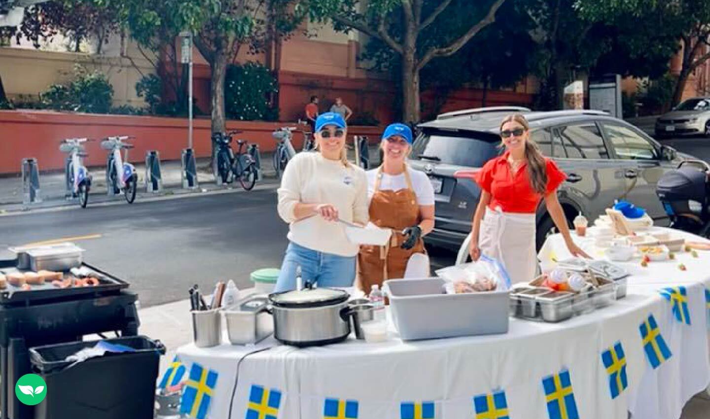 Amelia and her team pose behind their first street pop-up setup, featuring a Swedish flag–decorated table and hot dog prep station.