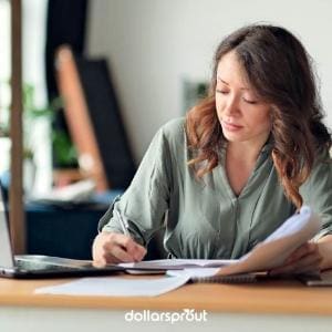 Woman working at a laptop with paperwork and coffee, representing the middle-class creator economy.
