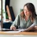 Woman working at a laptop with paperwork and coffee, representing the middle-class creator economy.