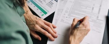 Person reviewing tax paperwork at a desk with a printed $400 Rule Made Simple chart nearby, illustrating when side hustlers owe self-employment tax. The image represents organizing finances and understanding the $400 tax threshold for freelancers and gig workers.